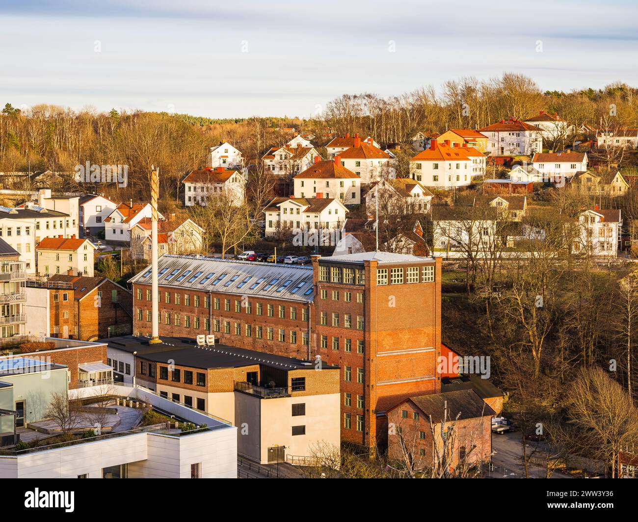 La lueur chaude du soleil couchant baigne le mélange de maisons résidentielles et d'installations industrielles à Mölndal, en Suède. La scène pittoresque met en valeur con Banque D'Images