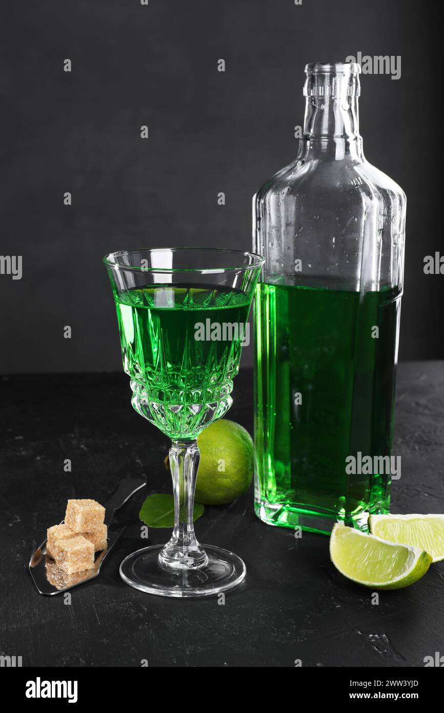 Absinthe, cuillère, cassonade et citron vert sur table noire. Boisson alcoolisée Banque D'Images