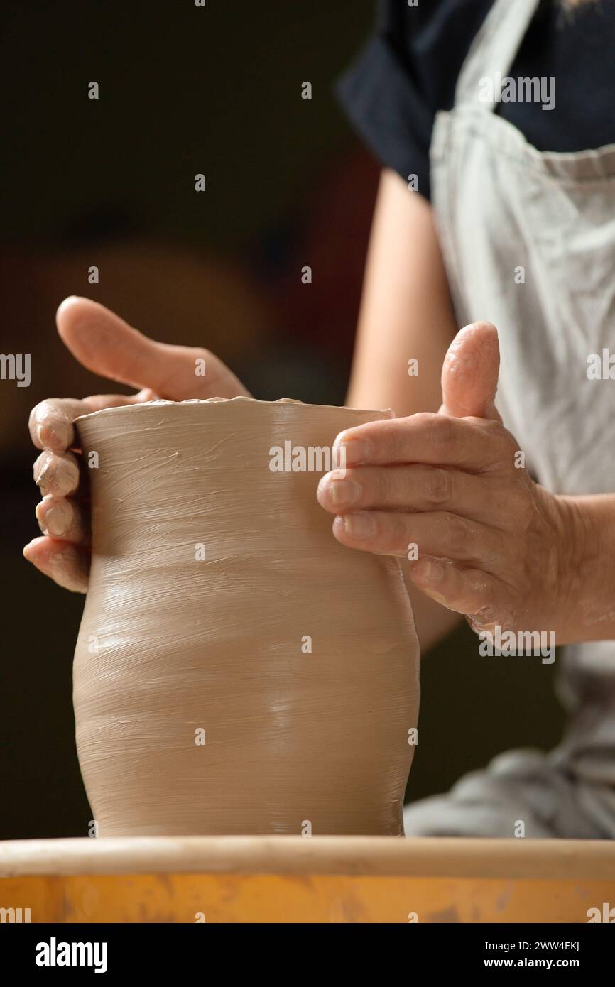 Les mains d'une femme travaillent sur une roue de potier, créant un vase ou un bol en céramique dans le studio. Hobbies, créativité, poterie. Produit en argile Banque D'Images