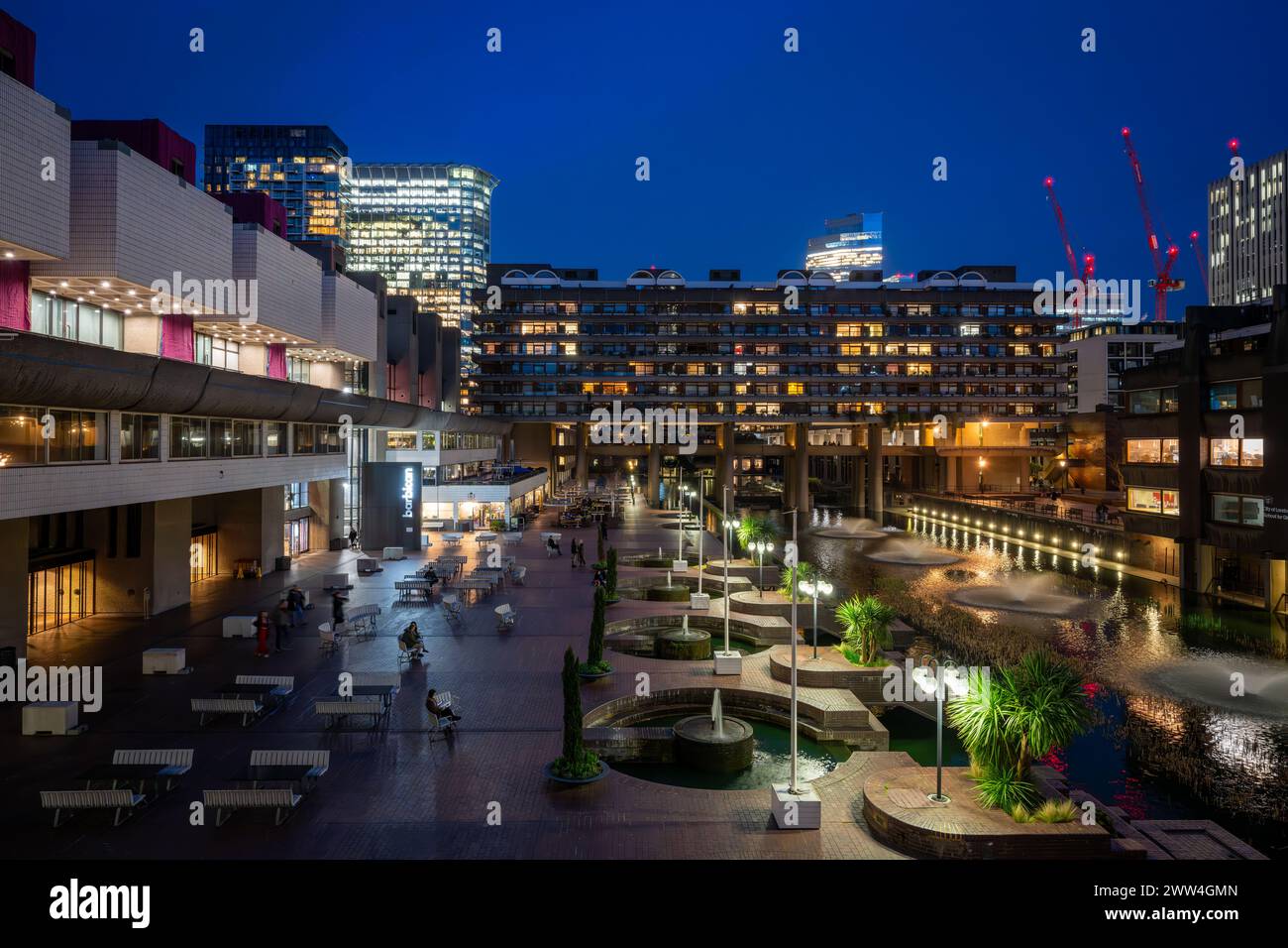 Londres, Royaume-Uni : vue nocturne du domaine Barbican dans la ville de Londres avec lac et fontaines. Un exemple éminent de l'architecture brutaliste. Banque D'Images