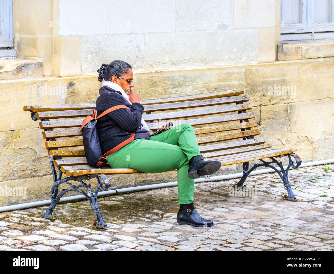 Femme noire française africaine assise sur un banc regardant un smartphone - Tours, Indre-et-Loire (37), France. Banque D'Images