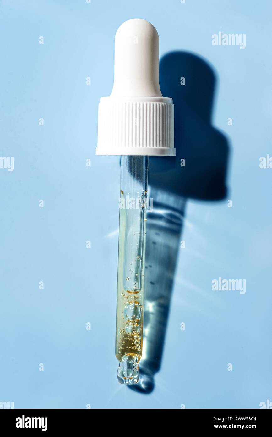 Pipette compte-gouttes avec sérum doré pour le visage ou gel de rétinol sur fond bleu gros plan. Soin de la peau avec acide ou peptide. Concept de tir cosmétique avec Sha dur Banque D'Images
