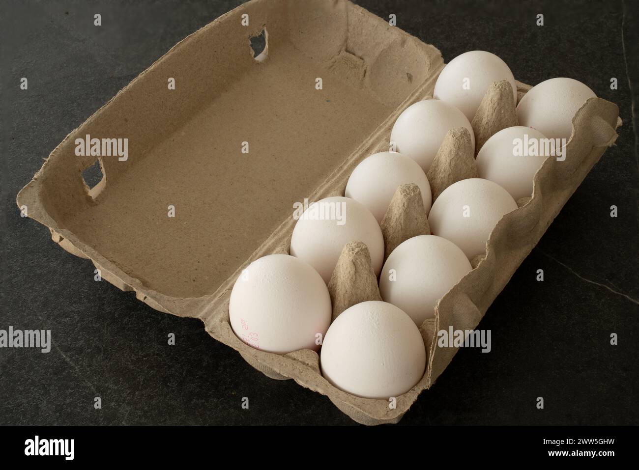 Faire dorer la boîte à œufs ouverte sur une table sombre avec dix œufs blancs dedans. Banque D'Images