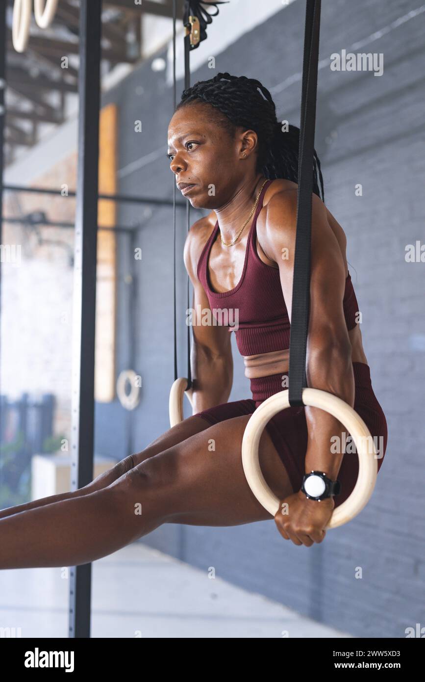 Une femme afro-américaine d'âge moyen en forme forte montre de la force sur les anneaux de gymnastique dans le gymnase Banque D'Images