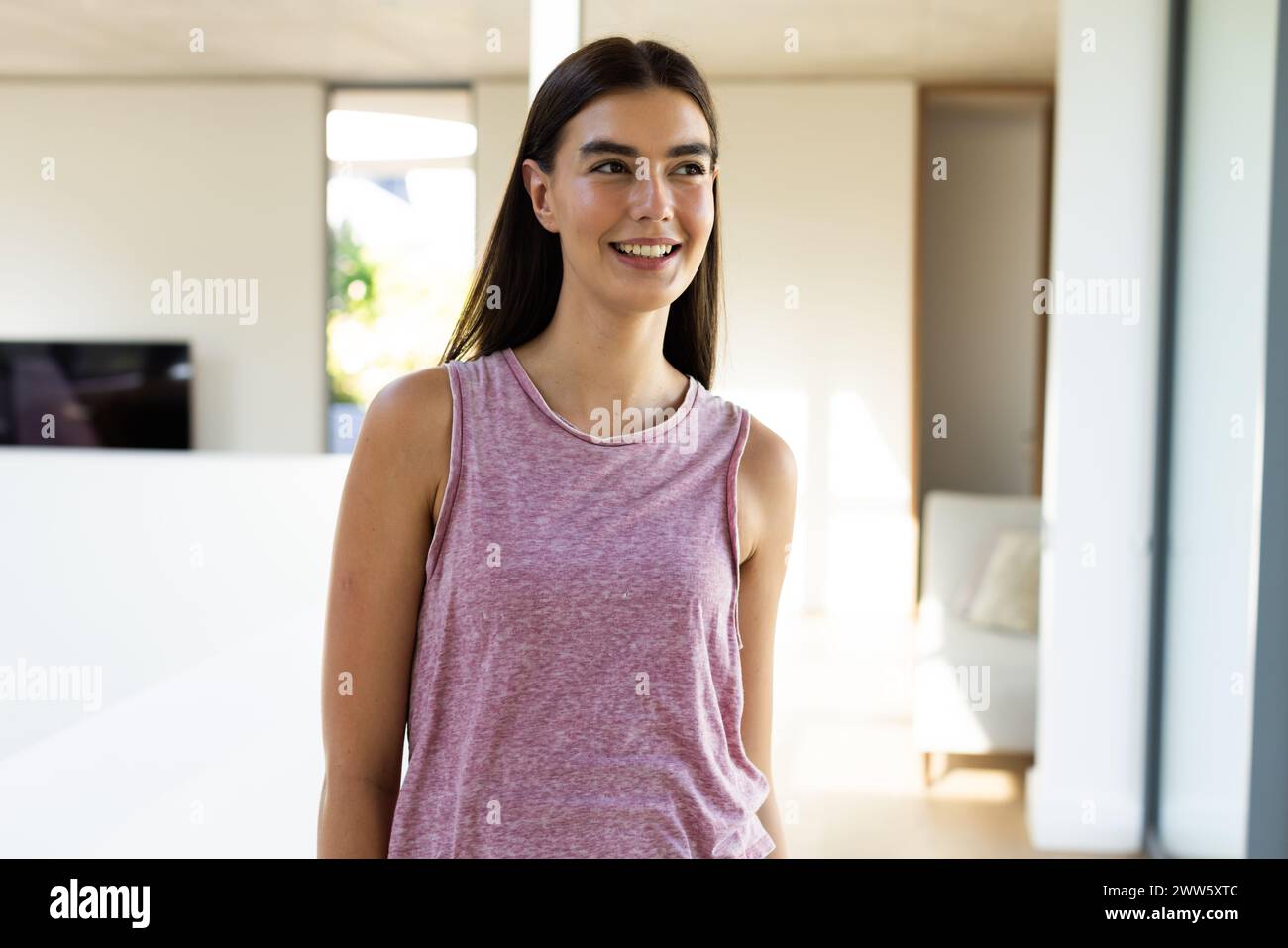 Une jeune femme brune caucasienne se tient souriante dans une pièce lumineuse à la maison Banque D'Images