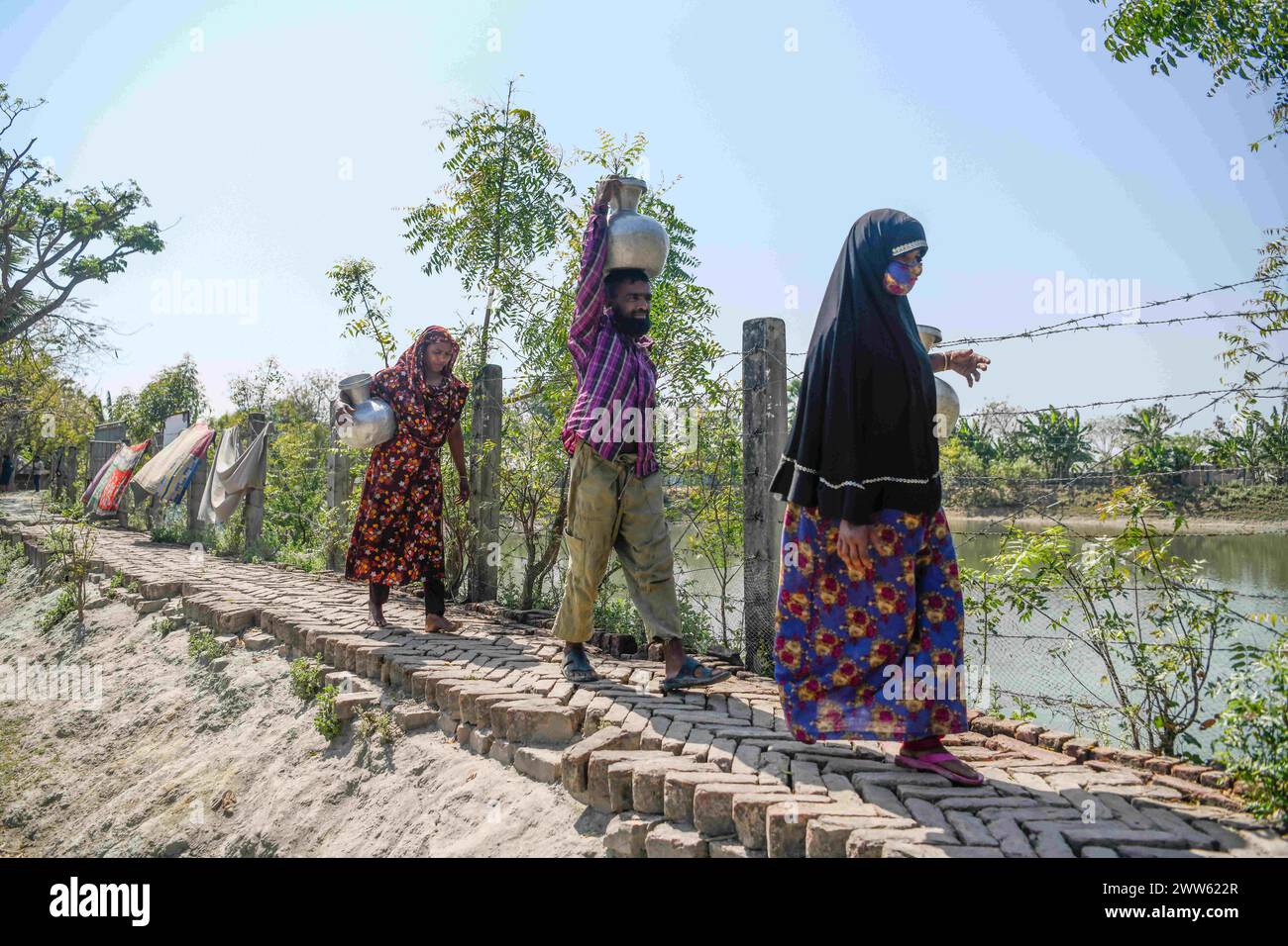 Dhaka, Bangladesh. 10 mars 2024. Personnes revenant de la collecte de l'eau potable d'un étang à Shyamnagar Gabura dans le district de Satkhira. À Gabura Union, dans le district de Shatkhira, dans le sud du Bangladesh, les habitants sont confrontés à une grave crise de l’eau potable exacerbée par le changement climatique. Les gens, y compris les femmes et les enfants, doivent parcourir quotidiennement de longues distances pour accéder à des sources d'eau salubre, ce qui augmente les risques sanitaires liés aux maladies d'origine hydrique. Les données au niveau des districts côtiers mettent en évidence des pourcentages significatifs aux prises avec des pénuries d'eau, les écologistes suggérant que la situation est plus grave. En déclin Banque D'Images