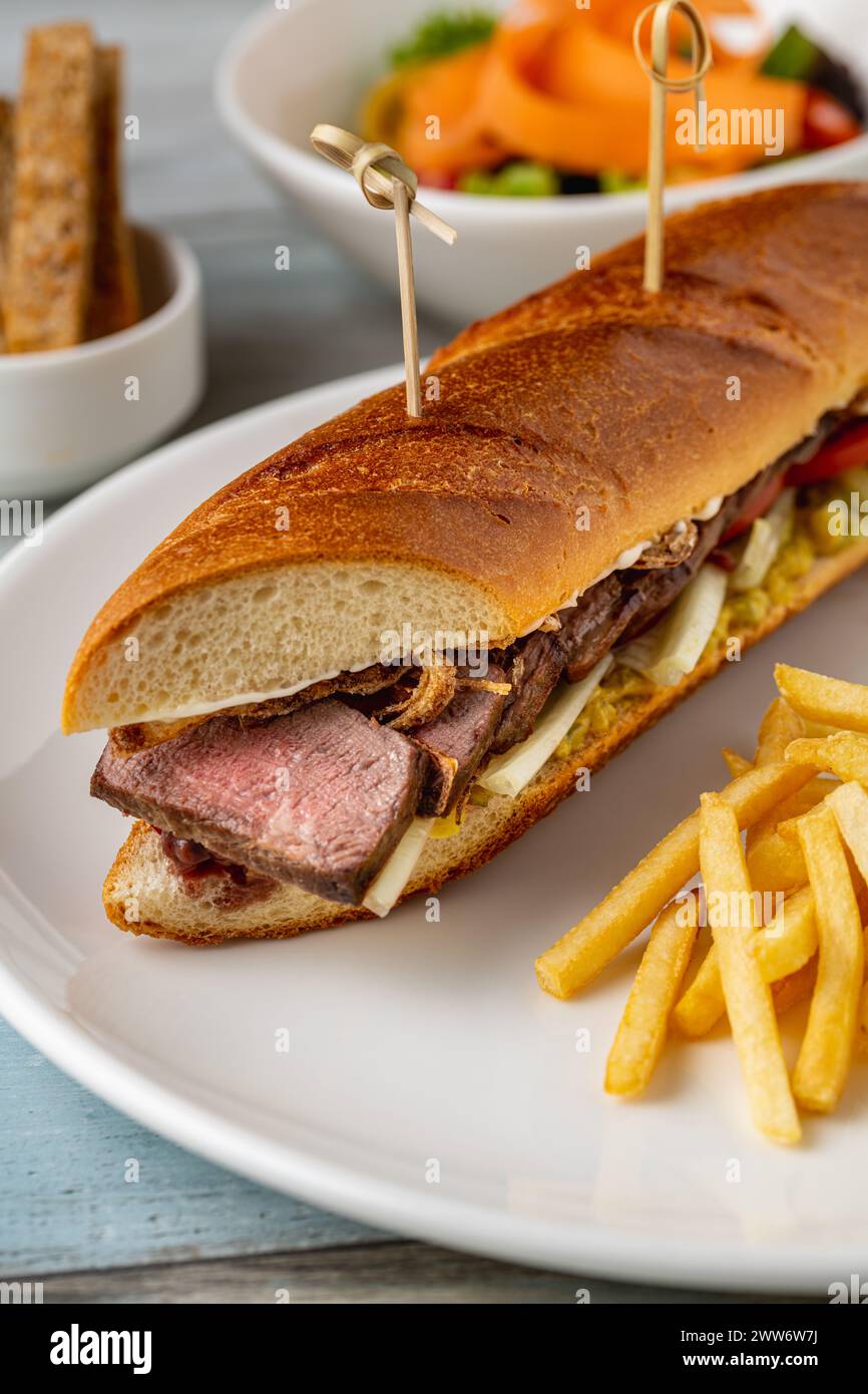 Sandwich au steak grillé avec frites sur une assiette en porcelaine blanche Banque D'Images