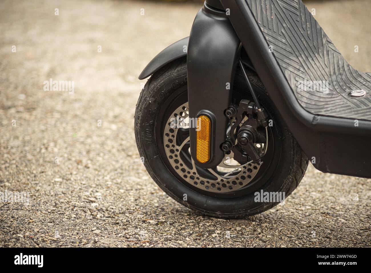 Un gros plan d'un pneu de scooter électrique noir sur une rue de ville. Banque D'Images