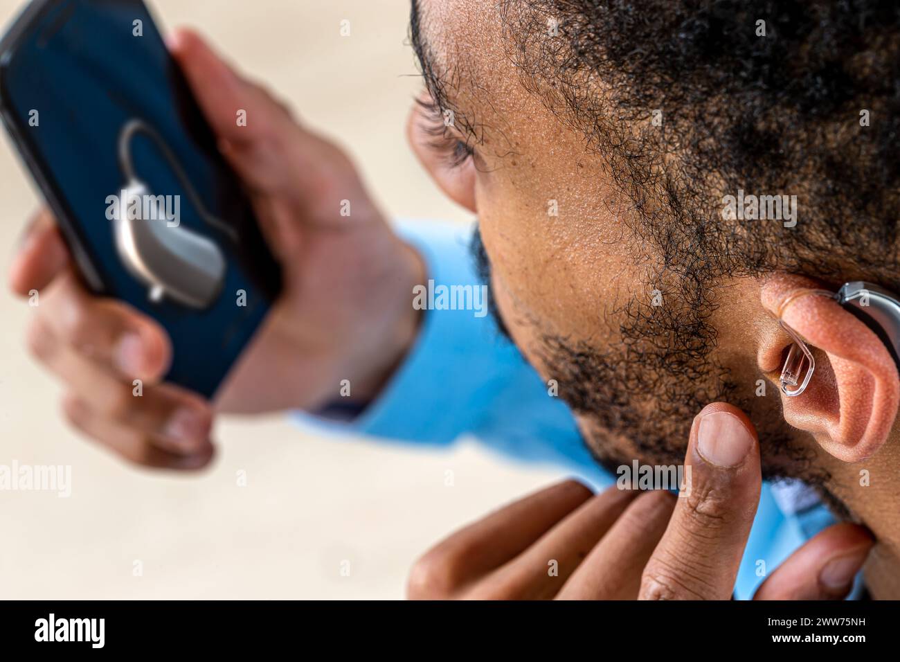 Jeune homme ajustant l'intensité du volume de l'aide auditive avec le smartphone. Banque D'Images