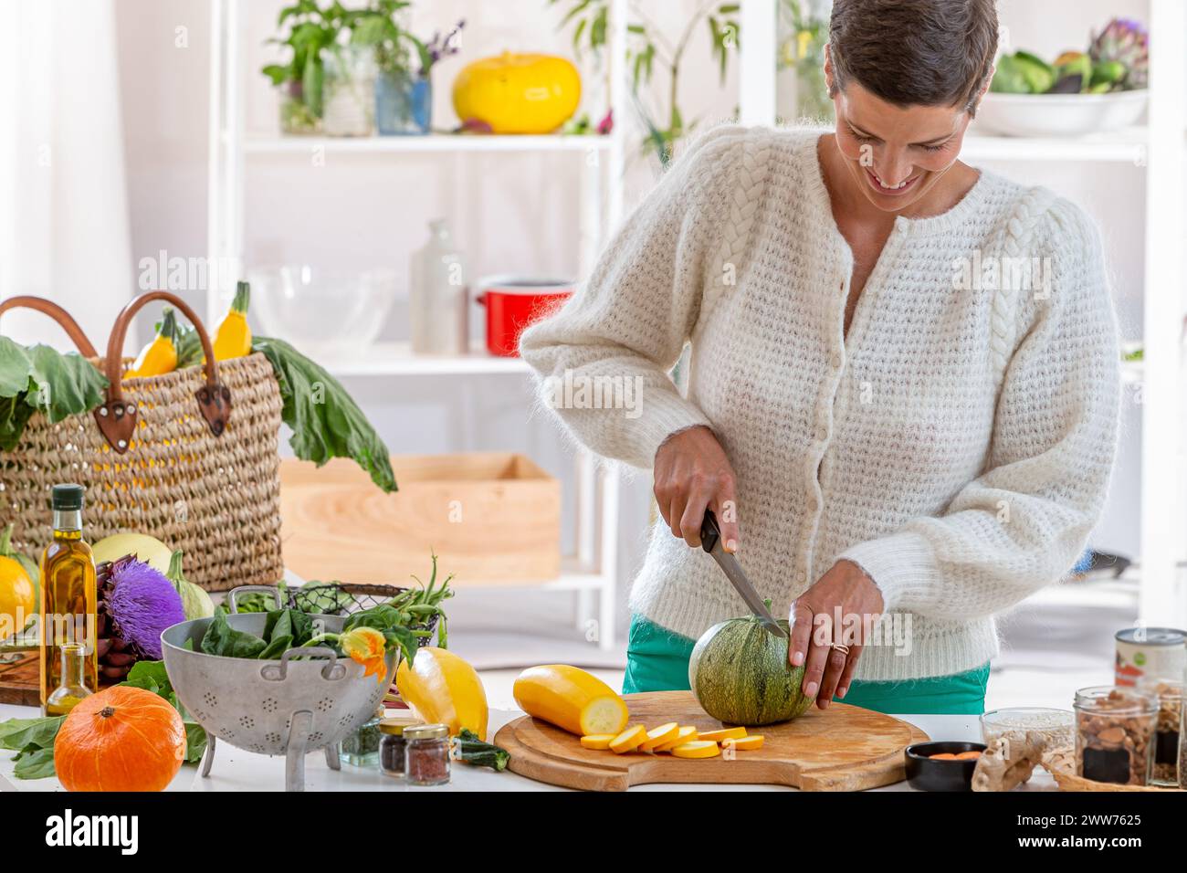 Jeune femme dans sa cuisine entourée de légumes biologiques. Banque D'Images