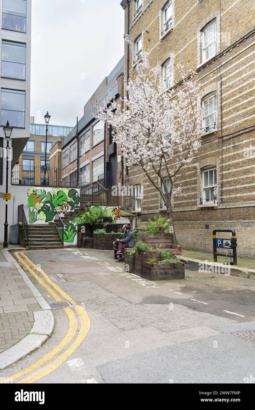 Une oasis urbaine tranquille à Londres. Une personne se détend au milieu des cerisiers en fleurs et de l'art de rue dynamique dans une ruelle cachée Banque D'Images