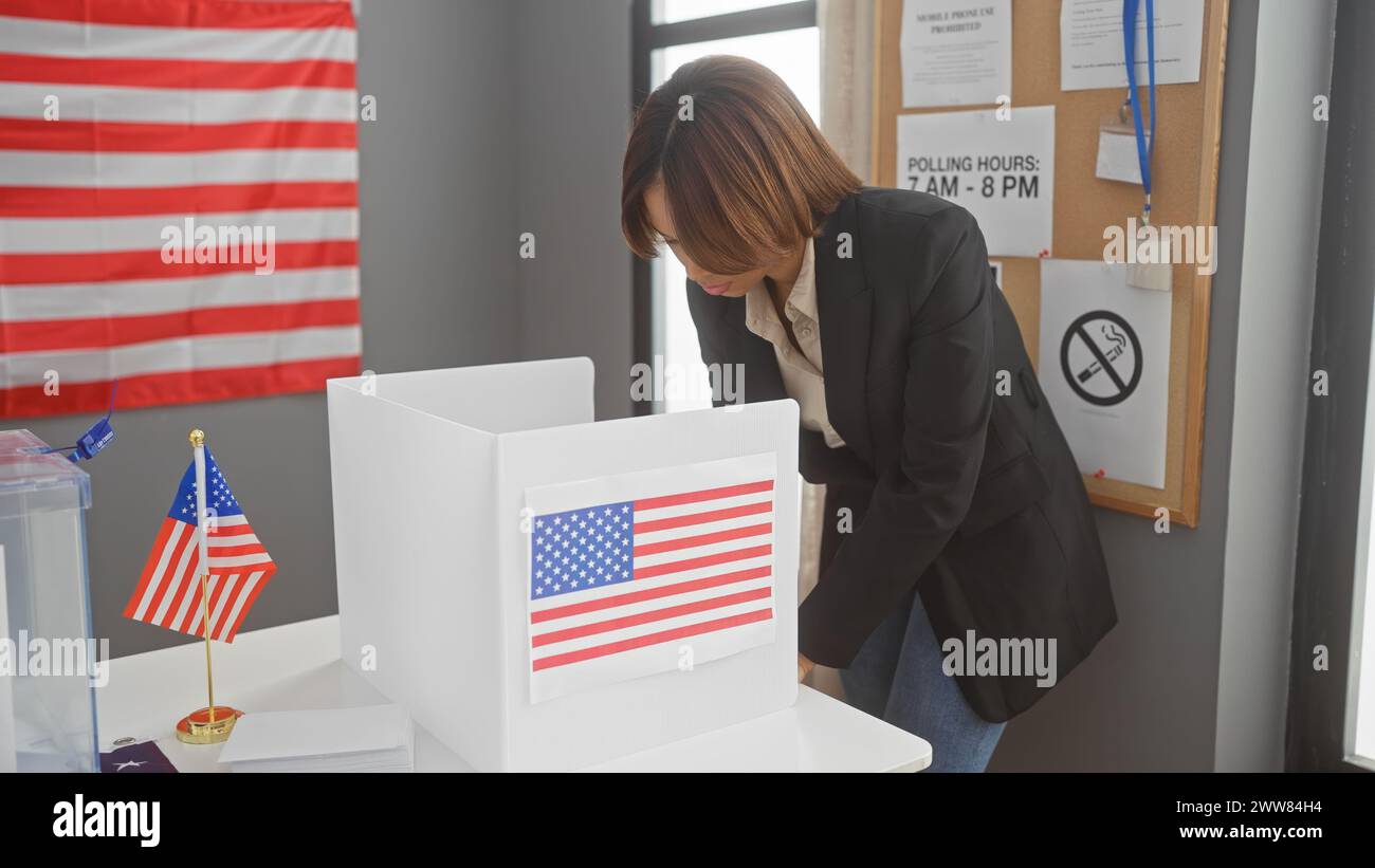 Femme afro-américaine votant à l'intérieur dans un établissement de collège électoral américain, avec des drapeaux américains en arrière-plan Banque D'Images