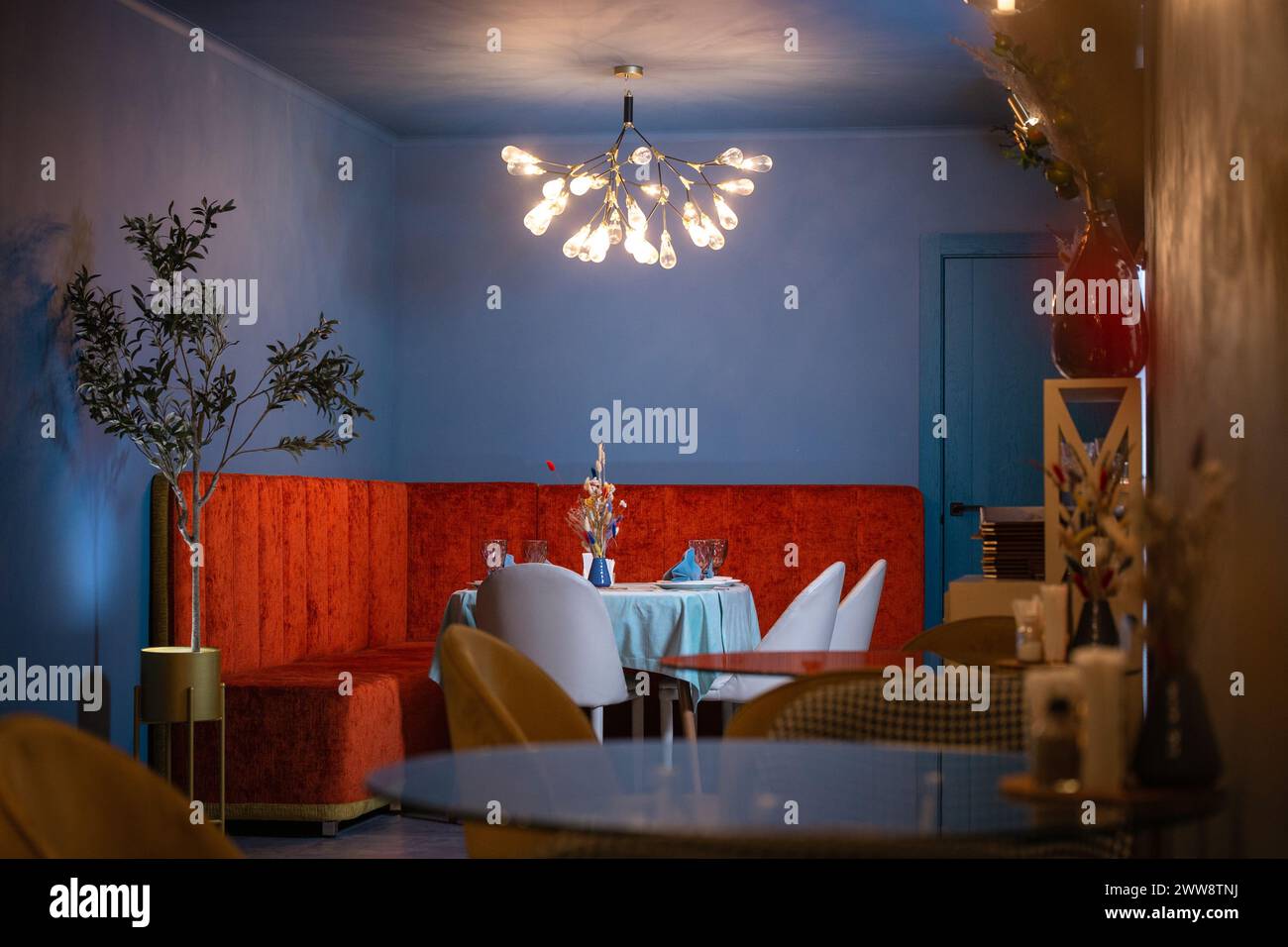 Un bel intérieur de restaurant avec des murs bleus et des meubles en velours rouge. Le restaurant est éclairé par un beau lustre. Banque D'Images