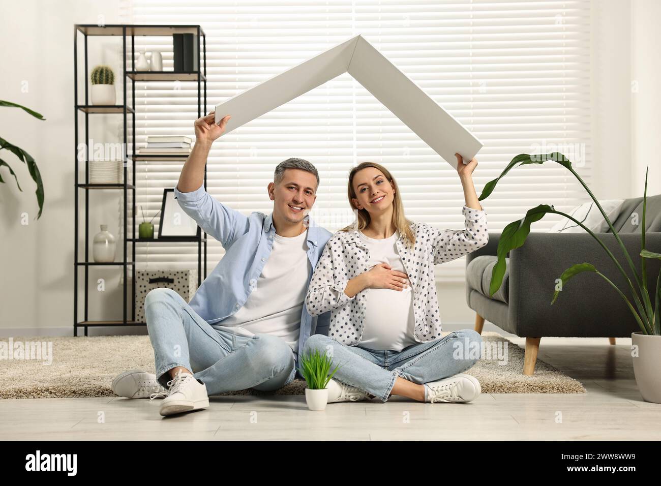 Concept de logement pour jeunes familles. Femme enceinte avec son mari assis sous un toit en carton sur le sol à la maison Banque D'Images