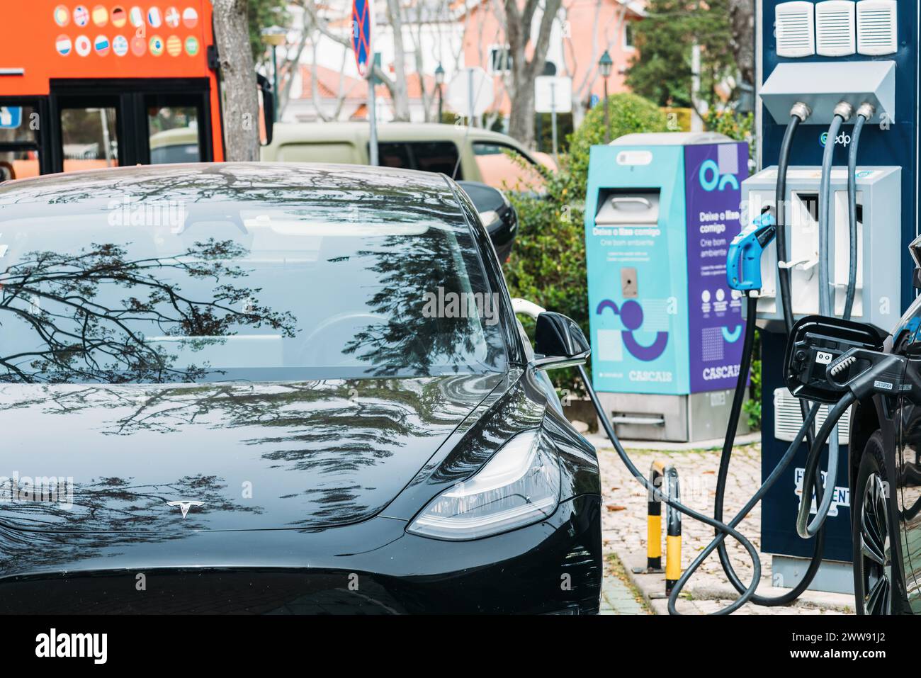 Cascais, Portugal - 22 mars 2024 : un véhicule électrique élégant est connecté à un compresseur Tesla au milieu d'un décor avec des arbres reflétant les voitures Banque D'Images