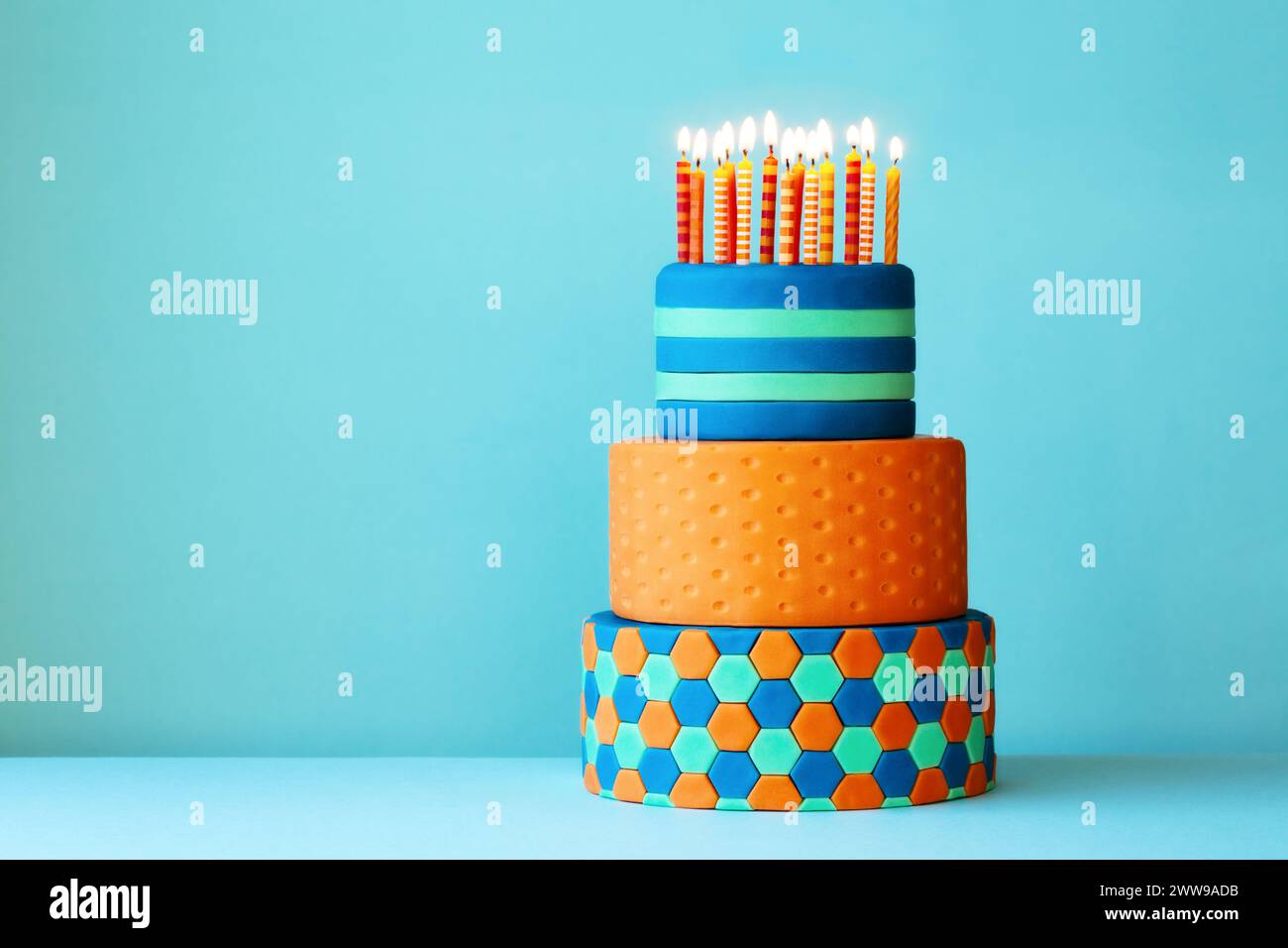 Gâteau d'anniversaire aux couleurs vives recouvert de fondant, trois niveaux et des bougies d'anniversaire colorées Banque D'Images