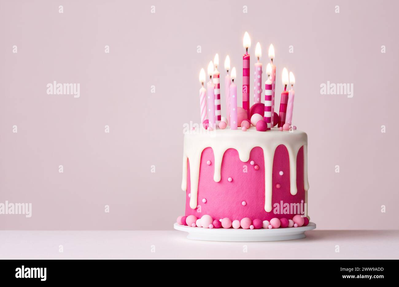 Gâteau d'anniversaire rose de célébration avec glaçage goutte à goutte et bougies d'anniversaire roses Banque D'Images
