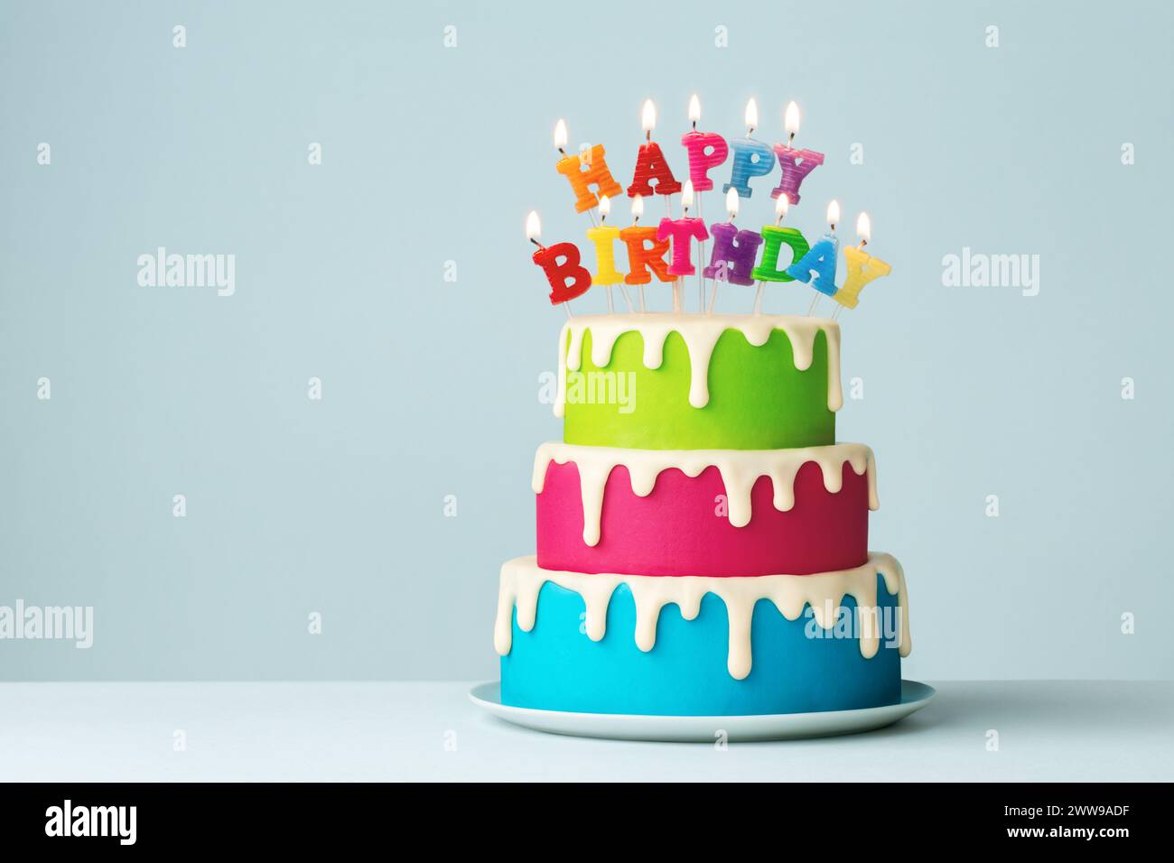 Gâteau d'anniversaire coloré à plusieurs niveaux avec des bougies colorées de joyeux anniversaire et du glaçage goutte à goutte Banque D'Images