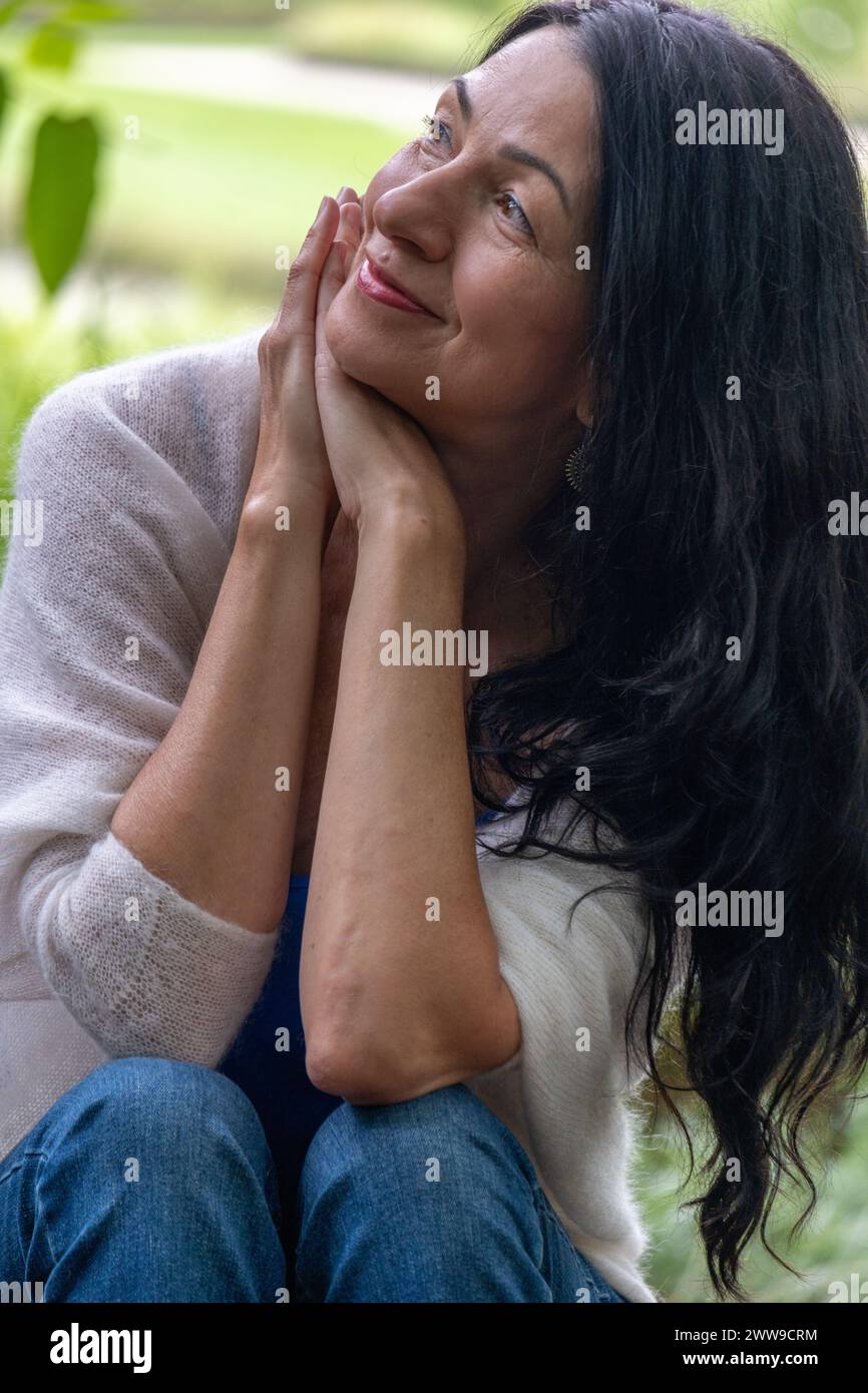 Capturée dans un moment de réflexion, cette image d’une femme souriante pourrait représenter des thèmes comme le bien-être mental, la joie de la solitude et la beauté O. Banque D'Images