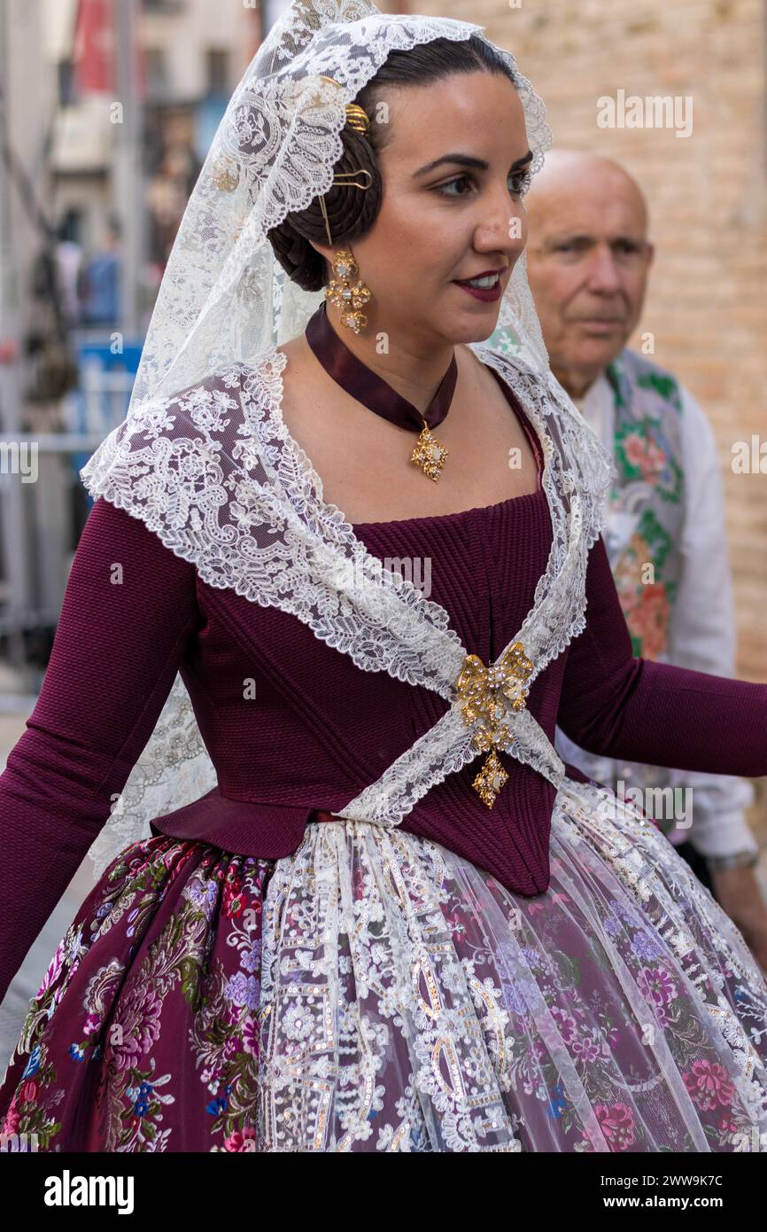 Splendeur festive valencienne ; la tenue dorée d'Une Fallera brille sur la toile de fond de la célébration. Sa robe Bordeaux, ornée de dentelle, capture le Banque D'Images