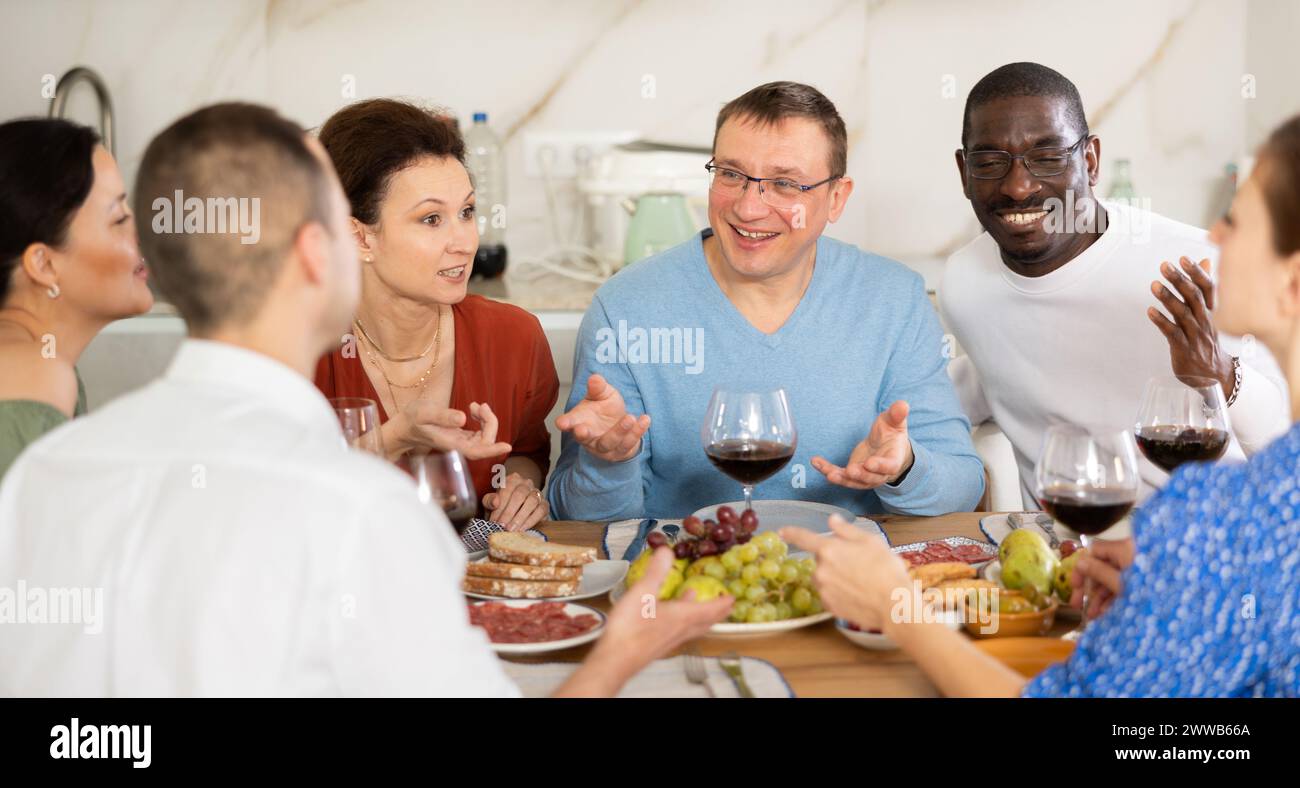 Les compagnons se sont rassemblés autour d’une table festive, participant à des discussions animées et dégustant les délices du vin rouge Banque D'Images