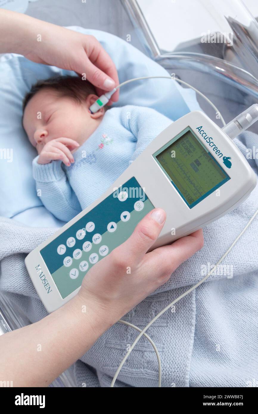 Hôpital. Maternité. Test auditif - Une infirmière de garde effectue un test auditif (test OAE - émissions otoacoustiques) sur un nouveau-né endormi. Banque D'Images