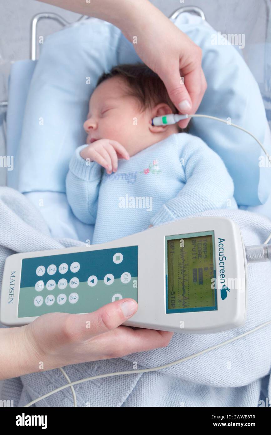 Hôpital. Maternité. Test auditif - Une infirmière de garde effectue un test auditif (test OAE - émissions otoacoustiques) sur un nouveau-né endormi. Banque D'Images