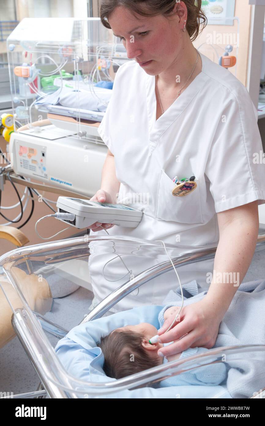 Hôpital. Maternité. Test auditif - Une infirmière de garde effectue un test auditif (test OAE - émissions otoacoustiques) sur un nouveau-né endormi. Banque D'Images
