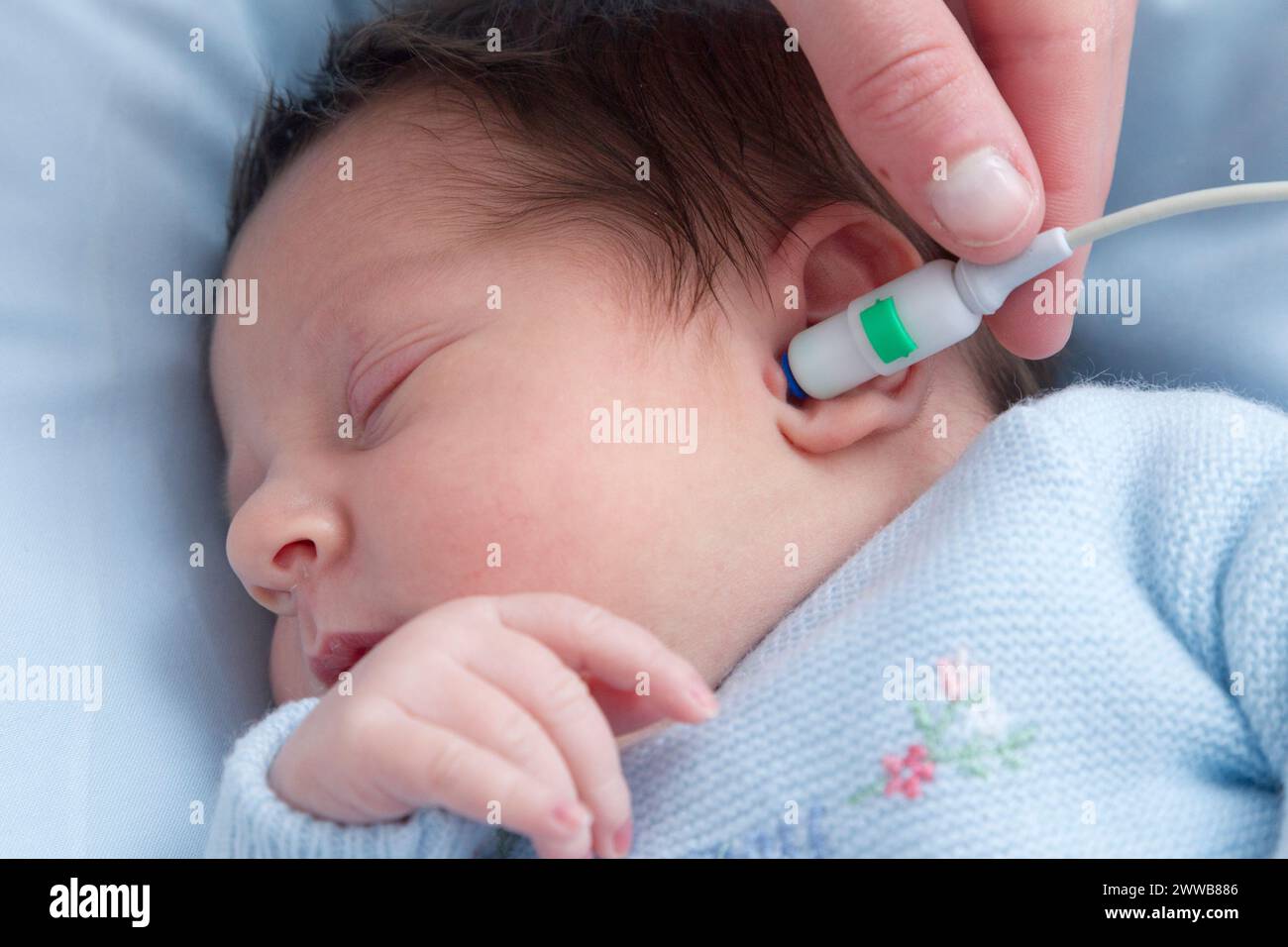 Hôpital. Maternité. Test auditif - Une infirmière de garde effectue un test auditif (test OAE - émissions otoacoustiques) sur un nouveau-né endormi. Banque D'Images
