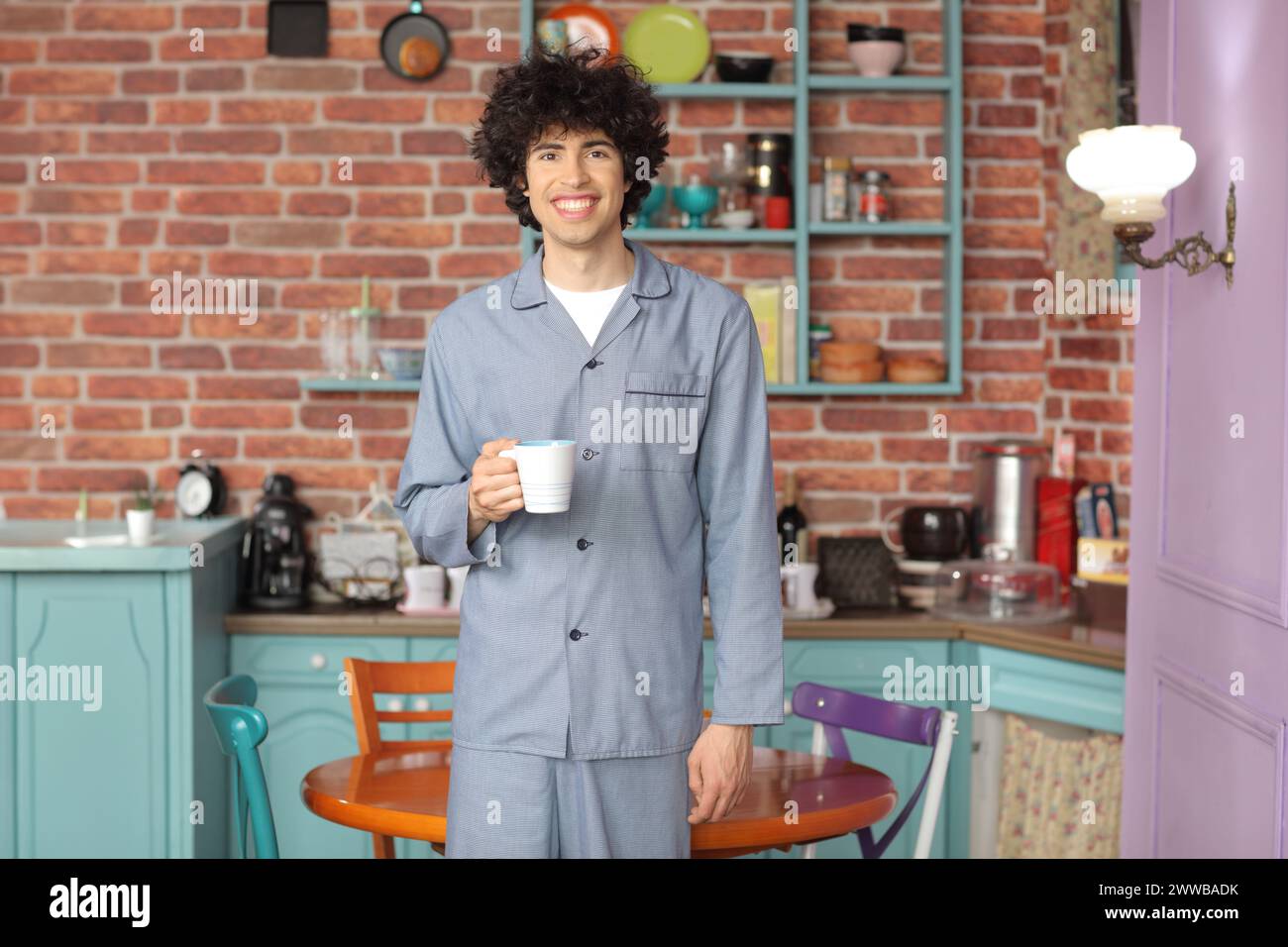 Jeune homme en pyjama tenant une tasse et debout dans une cuisine à la maison Banque D'Images