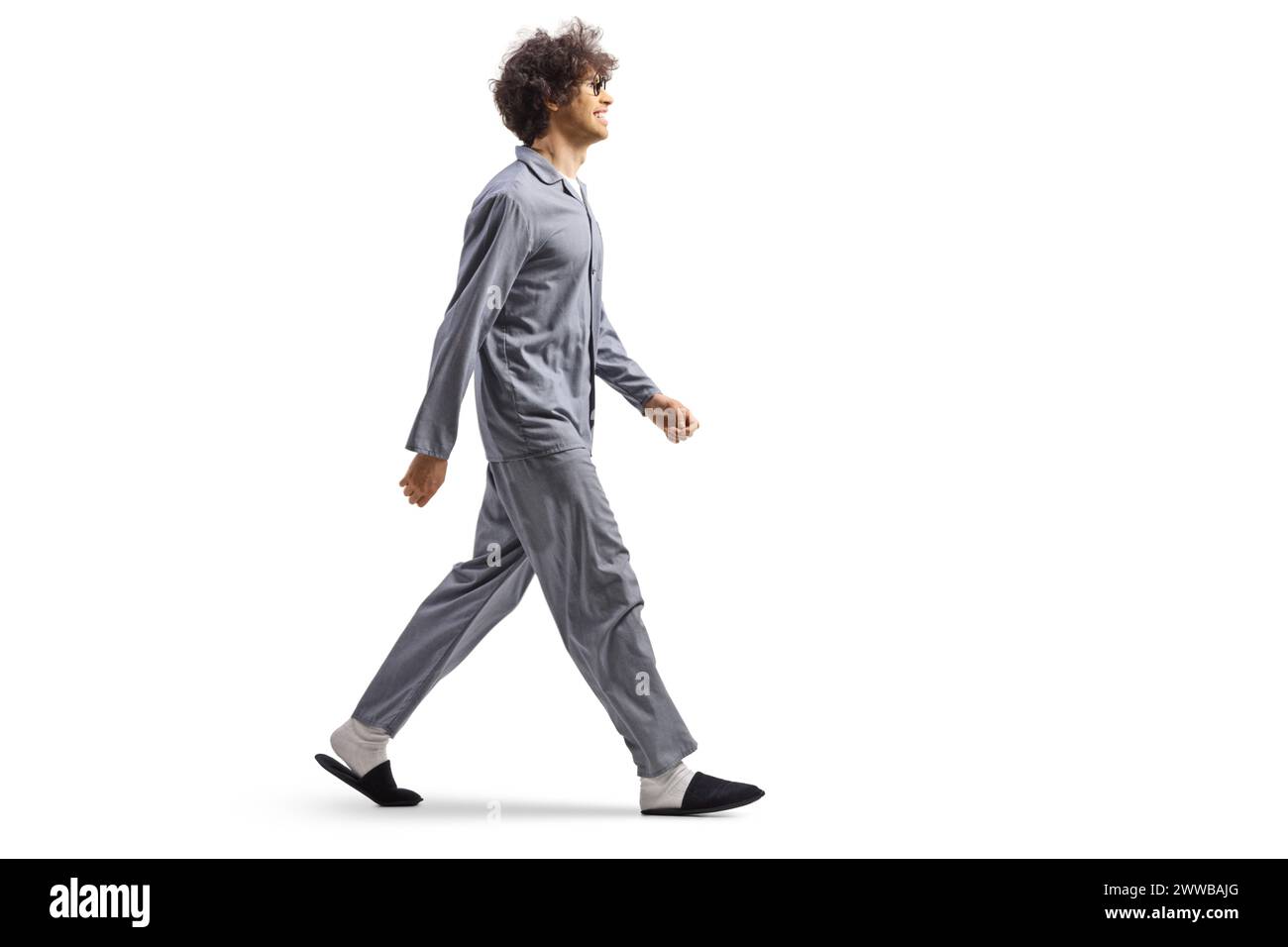 Plan de profil pleine longueur d'un jeune homme en pyjama et pantoufles marchant isolé sur fond blanc Banque D'Images