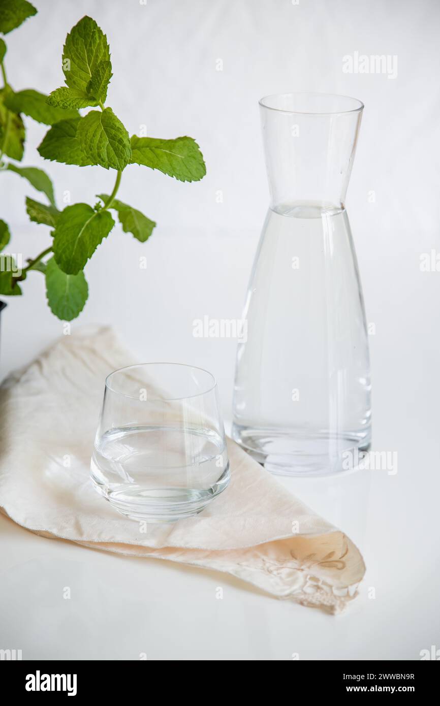 Tasse en verre et récipient avec de l'eau naturelle sur fond blanc. Image minimaliste, simple et propre. Concept de simplicité de l'eau potable. Banque D'Images