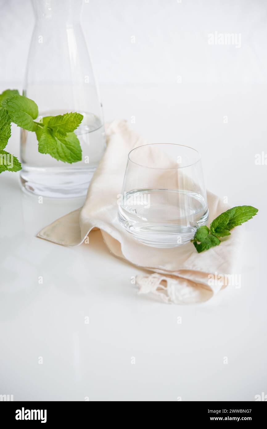 Tasse en verre et récipient avec de l'eau naturelle sur fond blanc. Image minimaliste, simple et propre. Concept de simplicité de l'eau potable. Banque D'Images