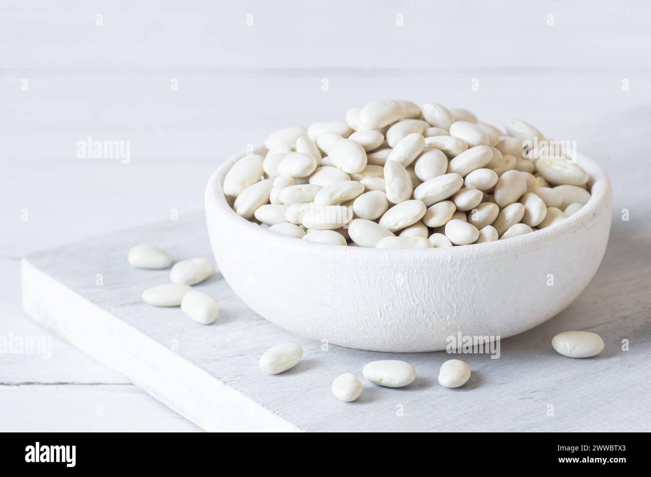 Haricots blancs séchés non cuits dans un bol ou une cuillère sur la table. Tas de légumineuses haricots de fond ( Phaseolus vulgaris ) Banque D'Images