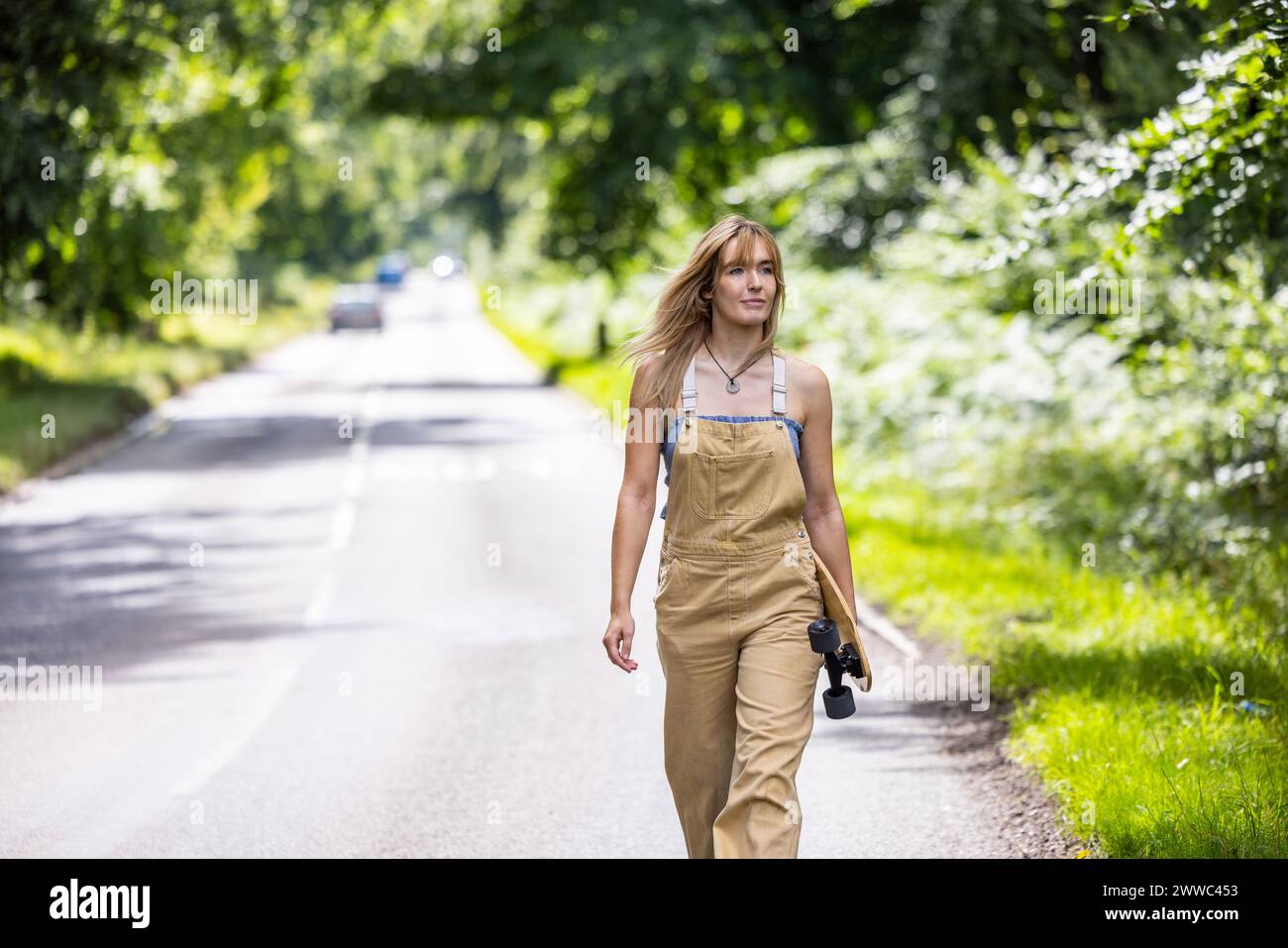 Jeune femme marchant avec skateboard dans la forêt Banque D'Images