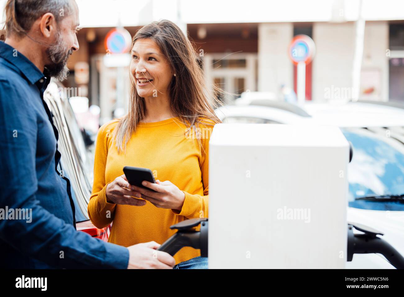 Couple heureux parlant à la station de charge de véhicule électrique Banque D'Images