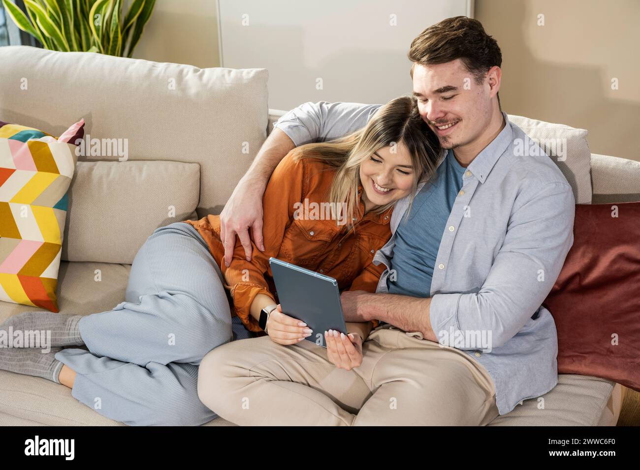 Aimer jeune couple en utilisant tablette PC sur canapé Banque D'Images