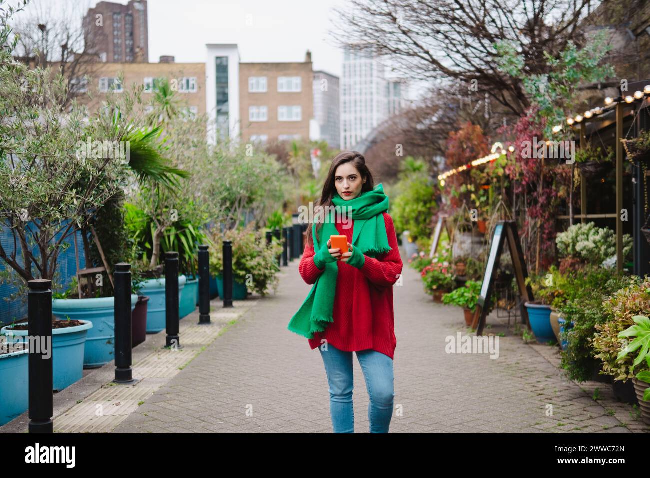 Femme tenant un téléphone intelligent et marchant sur un sentier dans la ville Banque D'Images