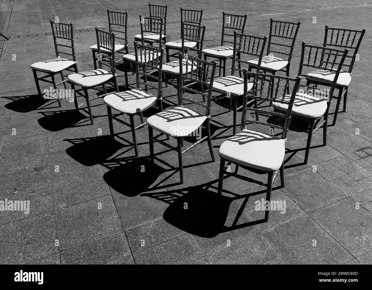 Sièges ensoleillés. Un défilé de 15 chaises sur la place de la ville. Lumière et ombre. Motif et texture. Noir et blanc, monochrome. Banque D'Images