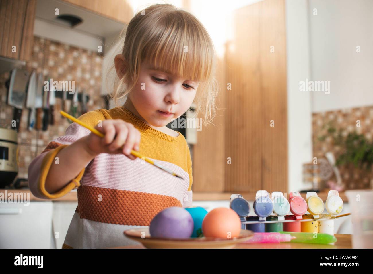 Jolie fille coloriant les oeufs de Pâques avec un pinceau à la maison Banque D'Images