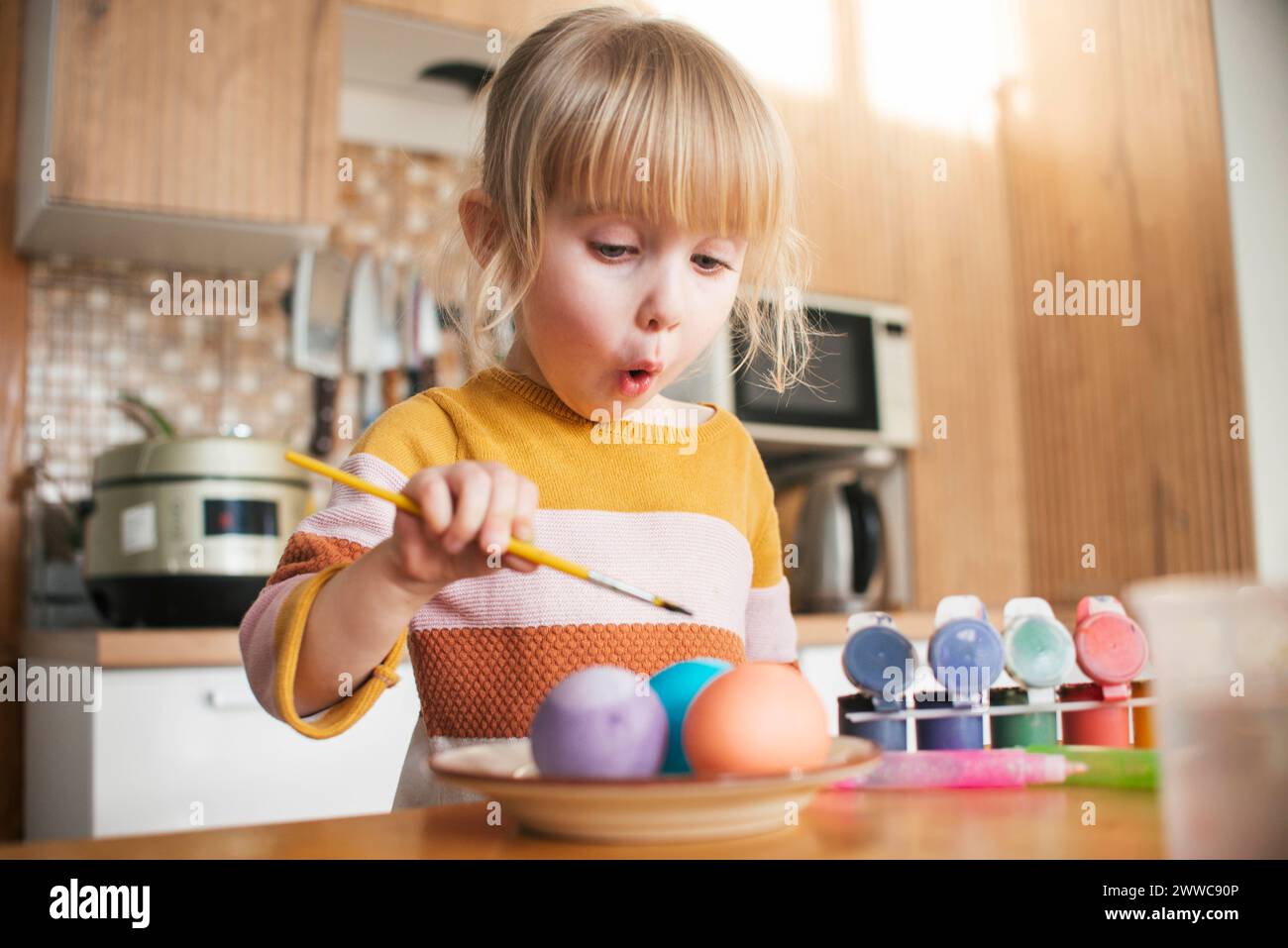 Fille surprise coloriant des œufs de Pâques avec un pinceau à la maison Banque D'Images