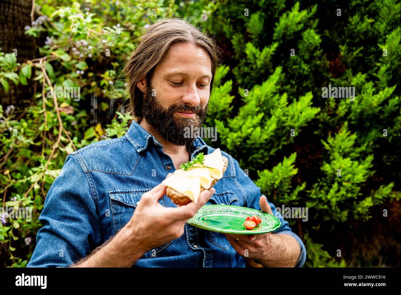 Homme à la barbe mangeant sandwich au fromage dans le jardin Banque D'Images