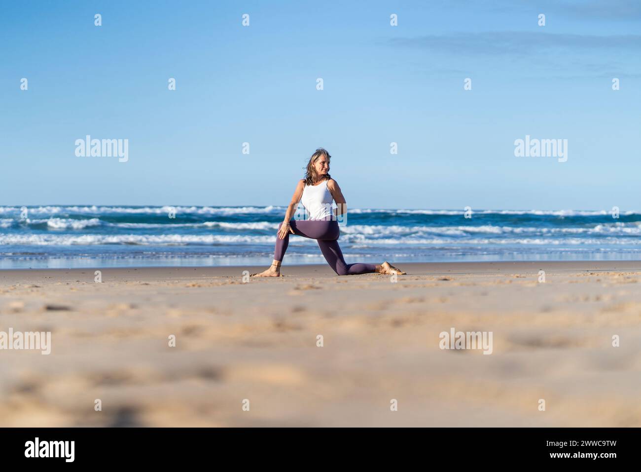 Femme mature pratiquant le yoga près de la mer sur la plage Banque D'Images