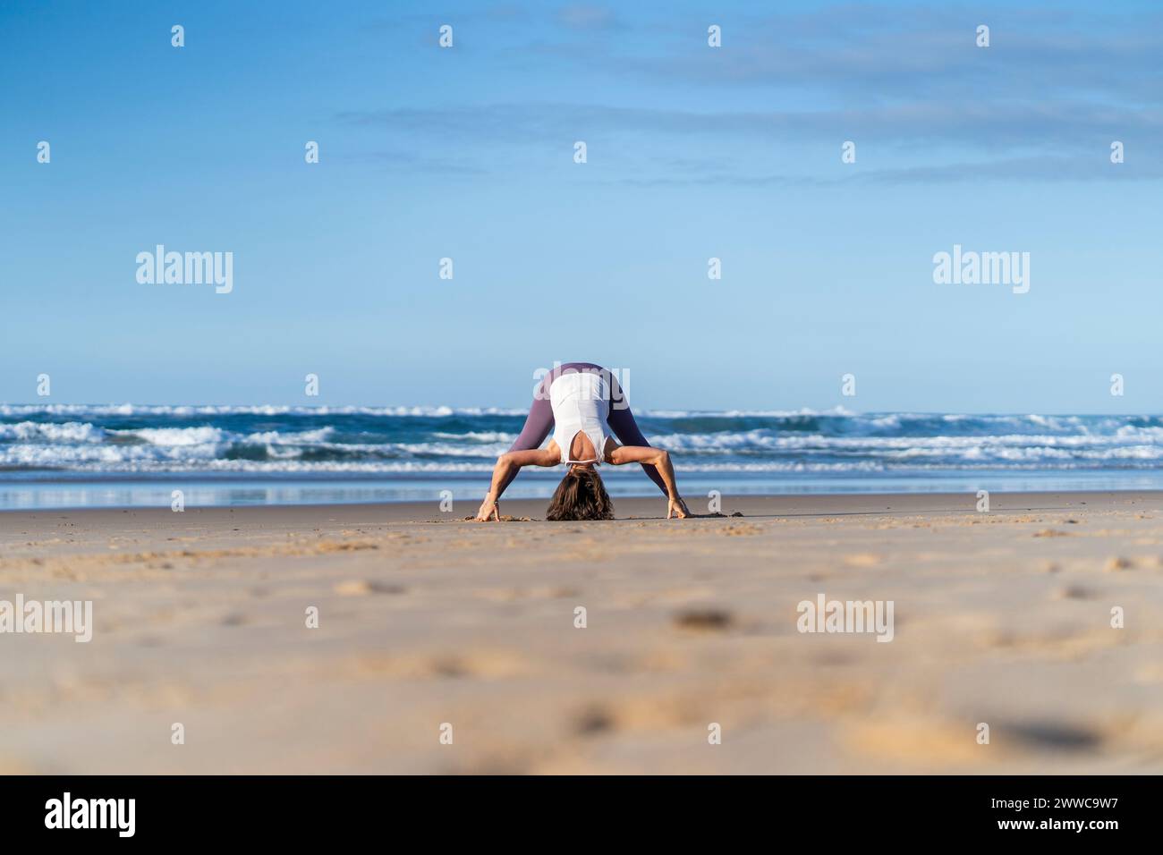 Femme se penchant et pratiquant le yoga près de la mer à la plage Banque D'Images