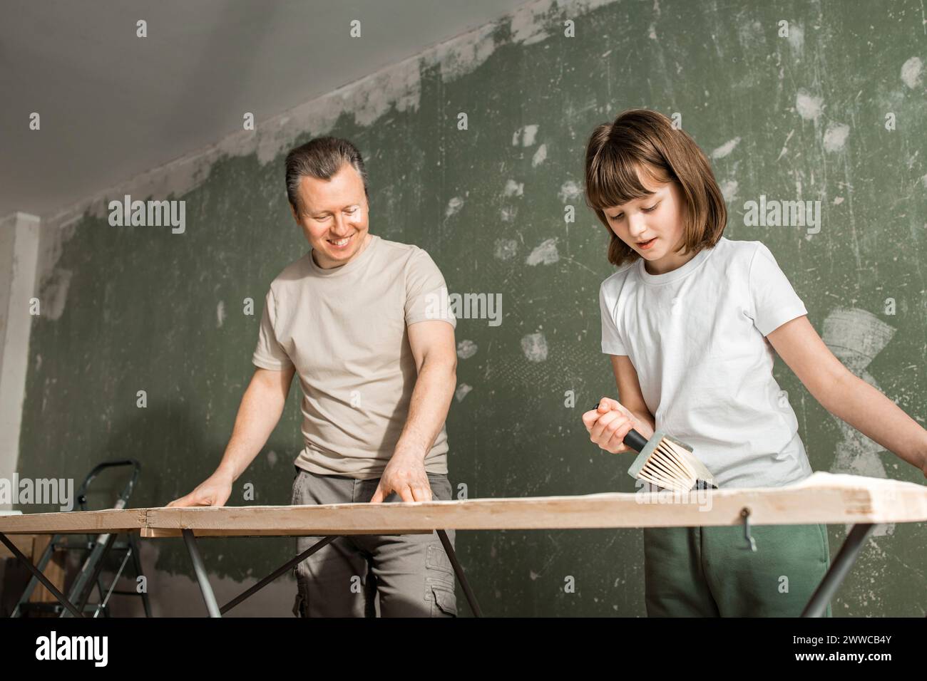 Heureux père et fille appliquant de la colle sur papier peint à la maison Banque D'Images