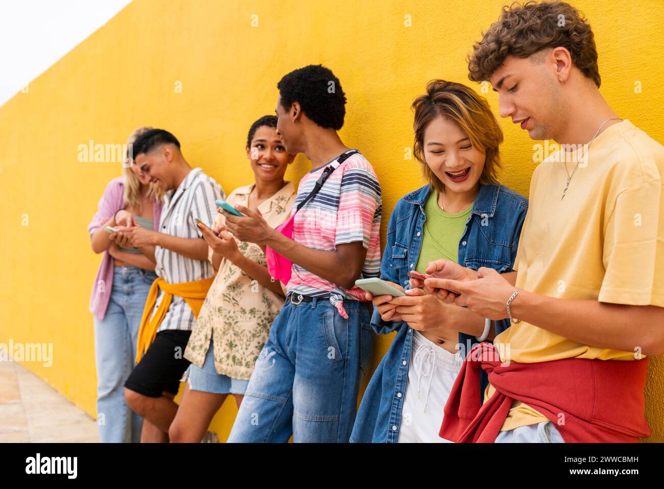 Groupe d'amis appuyés contre le mur jaune à l'aide de leurs téléphones intelligents Banque D'Images