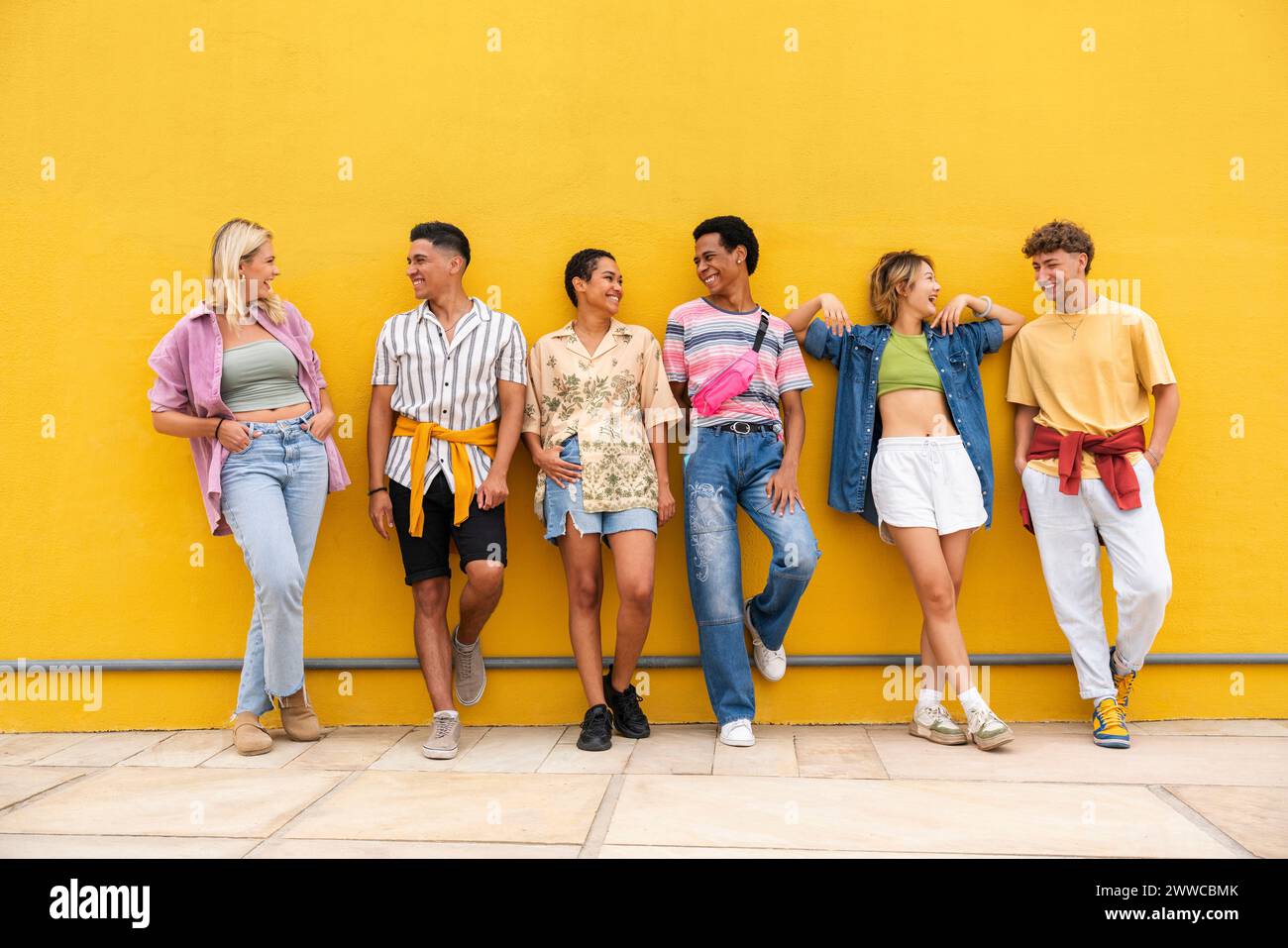 Amis insouciants dans des vêtements colorés bavardant dans le fronzt du mur jaune Banque D'Images