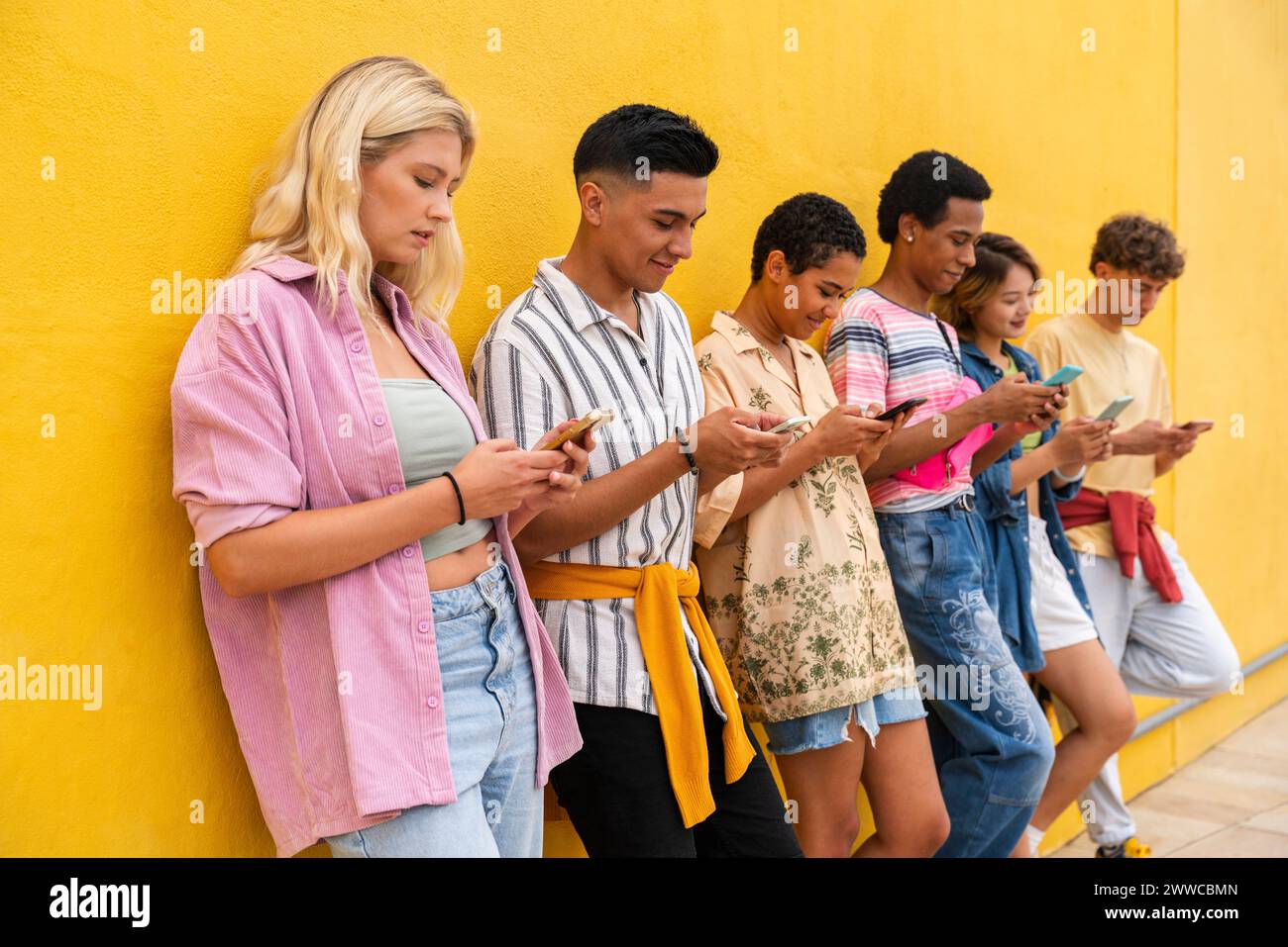 Groupe d'amis appuyés contre le mur jaune à l'aide de leurs téléphones intelligents Banque D'Images
