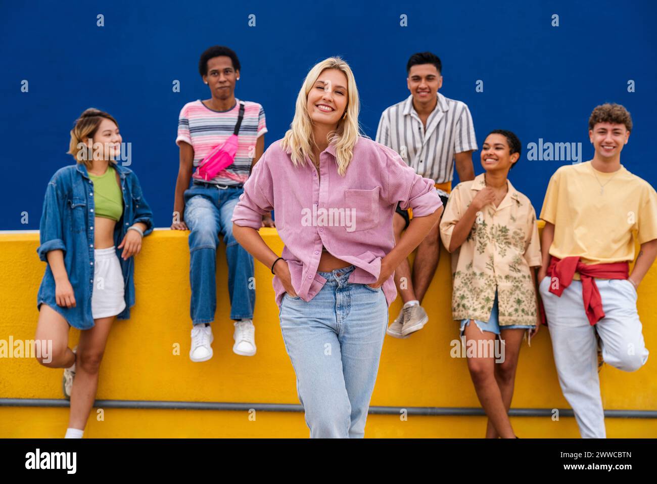 Femme blonde confiante debout devant un groupe d'amis avec les mains sur les hanches Banque D'Images
