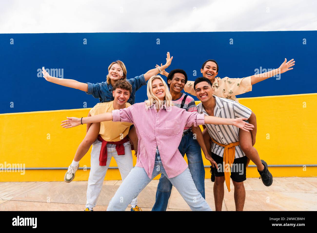 Groupe de jeunes amis avec des vêtements colorés posant joyeusement devant le mur Banque D'Images